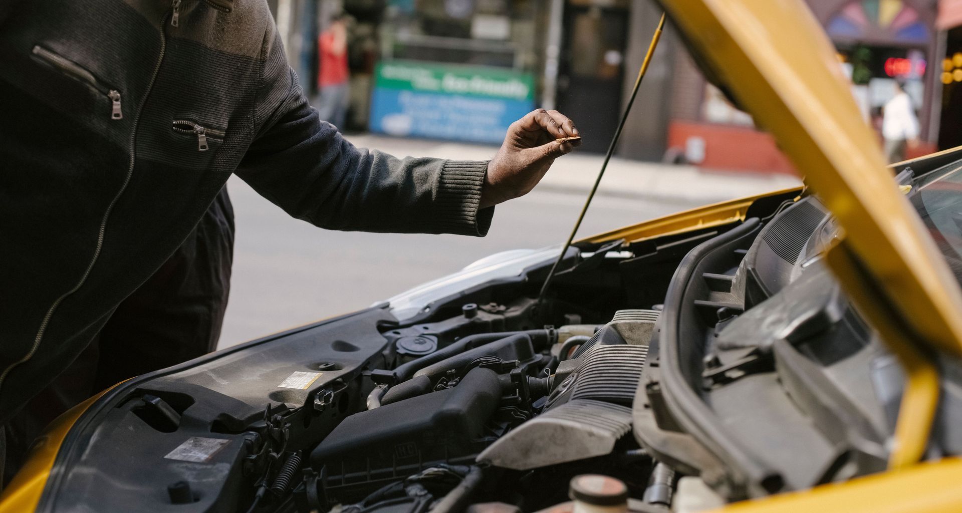 Side view of crop ethnic male repairing motor in broken auto parked on city street